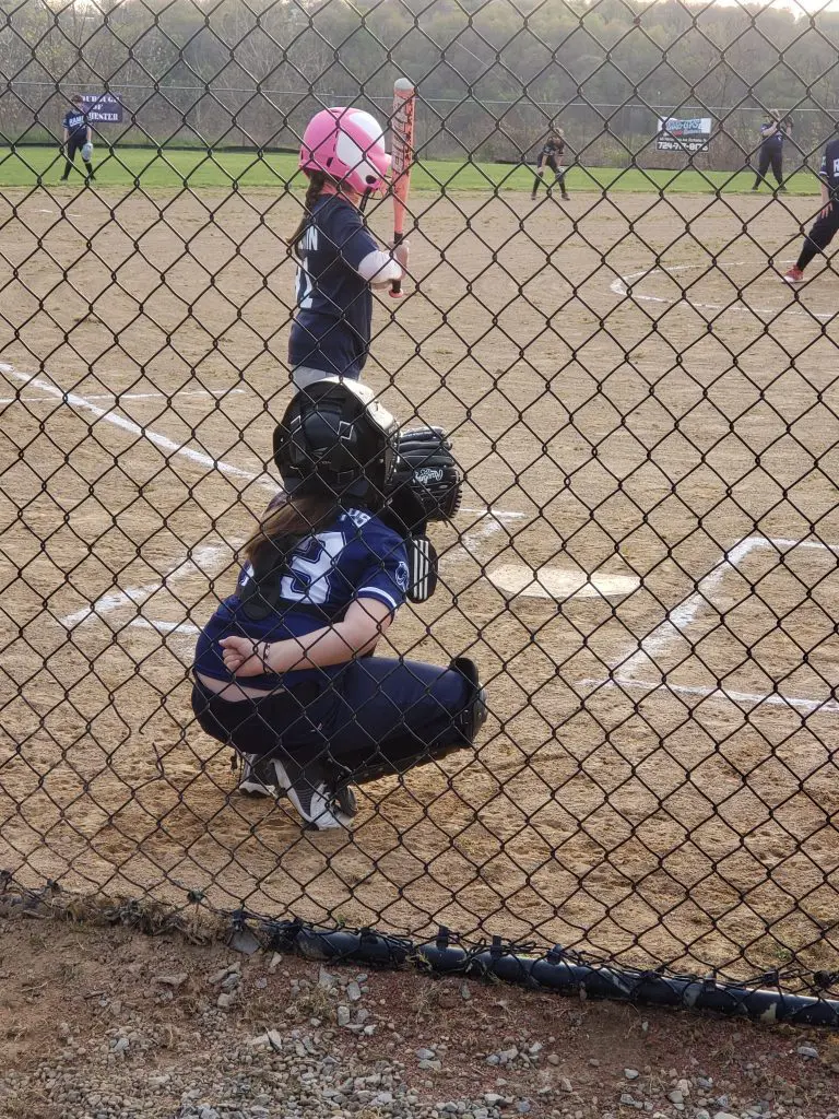 Rochester Area Youth Softball Association girl player athlete at bat on softball field with catcher ready to catch with All Kids Play financial assistance grant