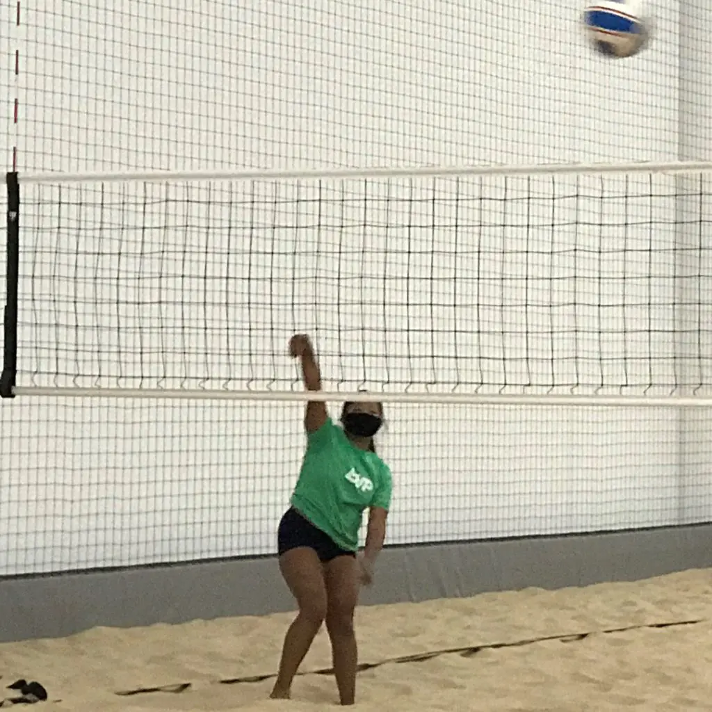 Girl beach volleyball athlete hitting a beach volleyball over the net on a sand court from All Kids Play grant