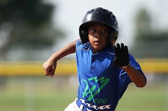 African American youth sports baseball player with batting helmet running the bases on a baseball field during a game