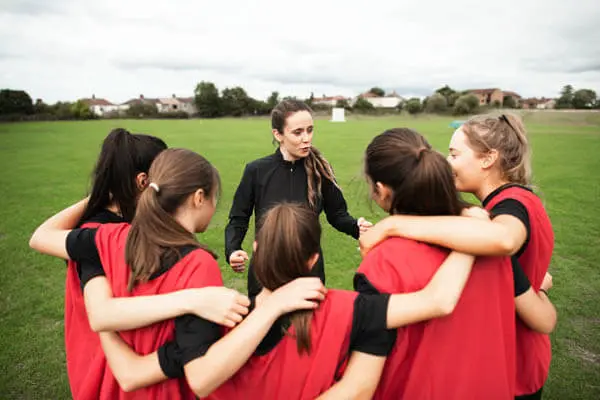 Female coach with youth sports girls soccer team in a huddle coaching and teaching during a game on a soccer field
