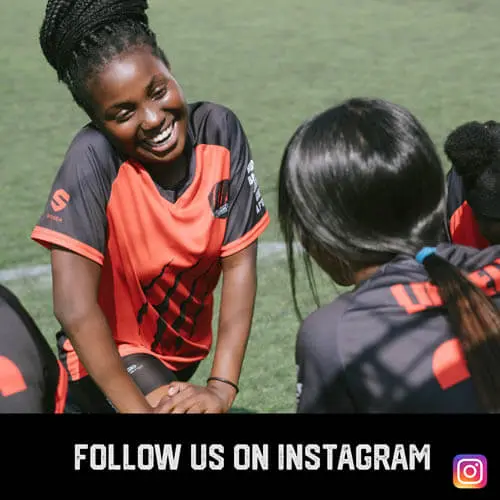 African American teenage girls youth sports soccer players stretching and laughing before a match on the field.