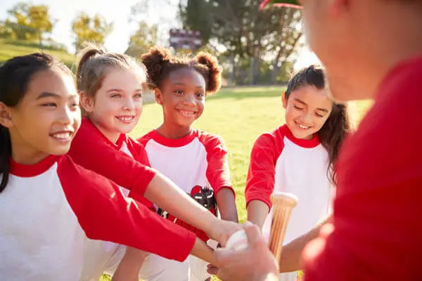 Multicultural diverse girls youth sports softball team with coach in huddle happy to play and coach teaching life skills and teamwork