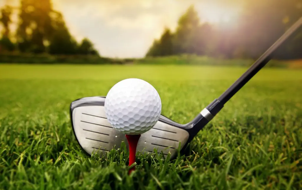 Golfer hitting a golf ball off a golf tee on a green for a charity golf outing event