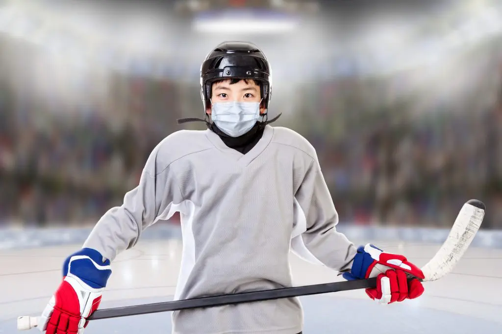 Asian youth male athlete hockey player with mask, stick and gear on hockey rink ice