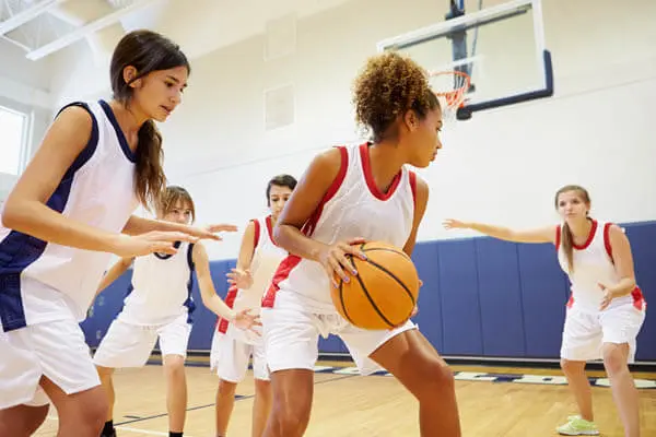 African American and Caucasian teenage girls youth sports basketball players practicing basketball in a scrimmage on a basketball court