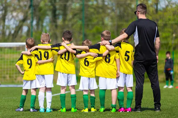 Boys youth sports soccer team and coach standing in partnership and teamwork on a soccer field