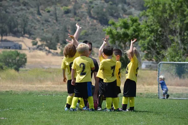 Coed youth sports soccer team in a huddle with coach hands raised asking questions on a soccer field