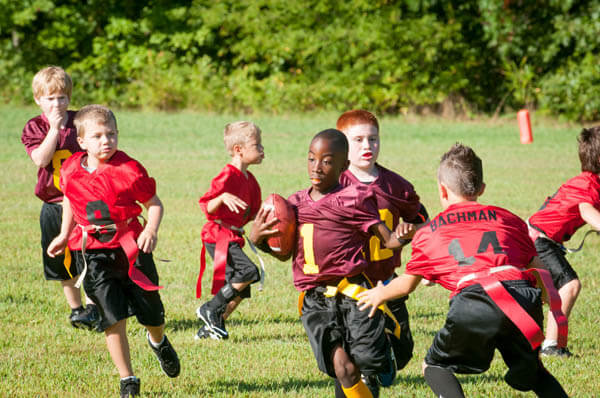 African American youth sports boy flag football player running against flag football team for a touchdown with a footbal on playing field
